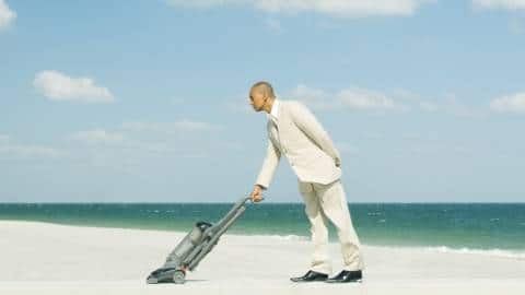 Un homme en train d'aspirer une plage de sable fin