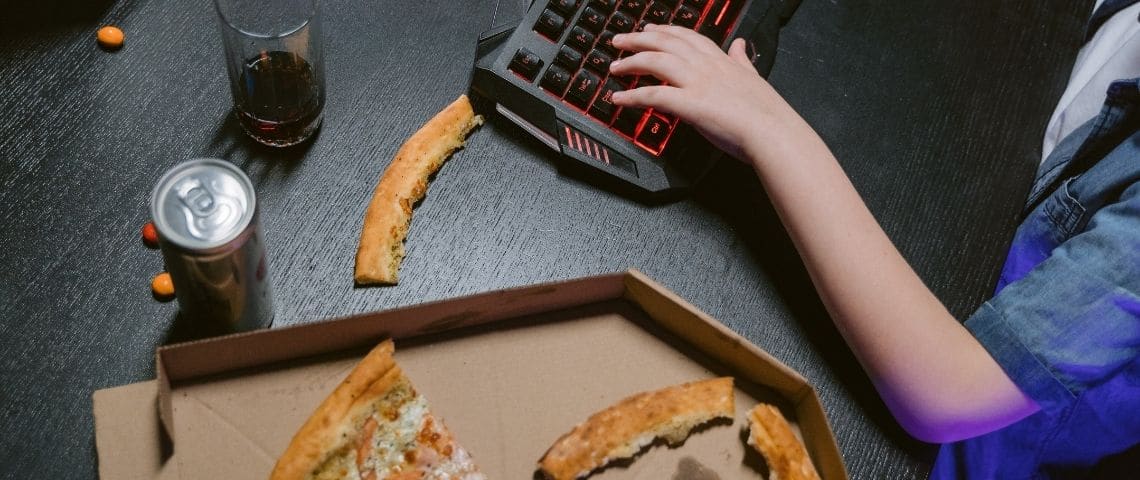 Jeu vidéo devient une marque unique globale et fait évoluer sa ligne éditoriale Main sur un clavier d'ordinateur, avec un verre de soda et une pizza entâmée posées à côté
