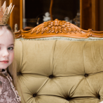 Une petite fille blonde avec une couronne sur la tête assise sur un divan vert