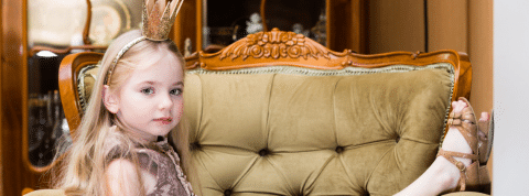 Comment les enfants sont devenus l'objet d'un culte narcissique Une petite fille blonde avec une couronne sur la tête assise sur un divan vert