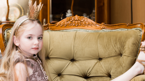 Une petite fille blonde avec une couronne sur la tête assise sur un divan vert