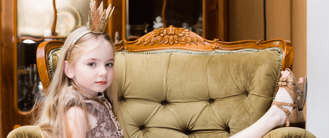 Comment les enfants sont devenus l'objet d'un culte narcissique Une petite fille blonde avec une couronne sur la tête assise sur un divan vert