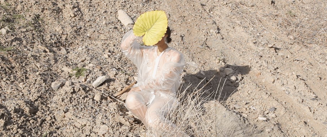 The Weight on the Land par Eve Tagny Dans le désert, une jeune femme au visage dissimulé par une grande feuille jaune