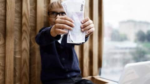 Un petit garçon devant un ordinateur brandit une liasse de billets
