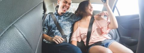 Oubliez les Uber et Airbnb à bas prix Deux jeunes adultes dans un Uber en train de prendre un selfie