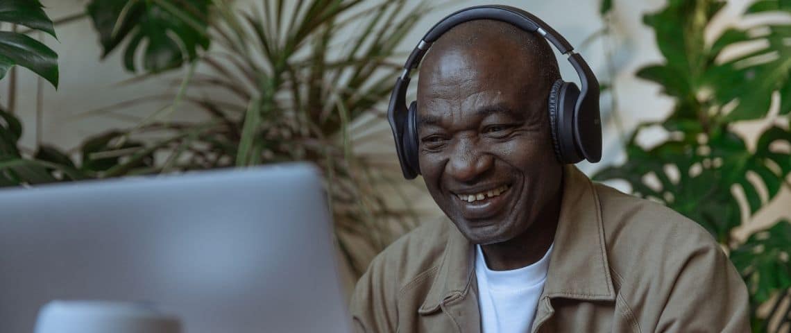 Prisma Media, Unify, M6 et Planet intègrent PrintAudioTM, la solution de text-to-speech d’Audion Homme avec un casque sur les oreilles, riant devant un ordinateur