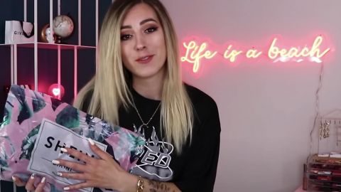 Une jeune fille blonde face tient un colis de la marque Shein