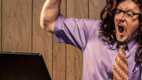 Un homme en chemise brandit le bras en criant face à son ordinateur