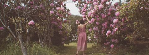Quand la mode réinvente son business model une femme en robe rose de dos dans l'herbe à côté d'arbres en fleurs