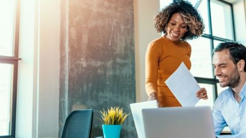 Une personne explique quelque chose à une autre devant un ordinateur.