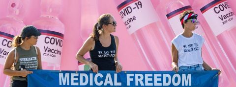 antivax Trois filles avec banderolle - Medical freedom - , avec en fond des doses de vaccins anti Covid