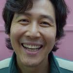 le visage d'un homme coréen souriant devant un mur rose, Squid games