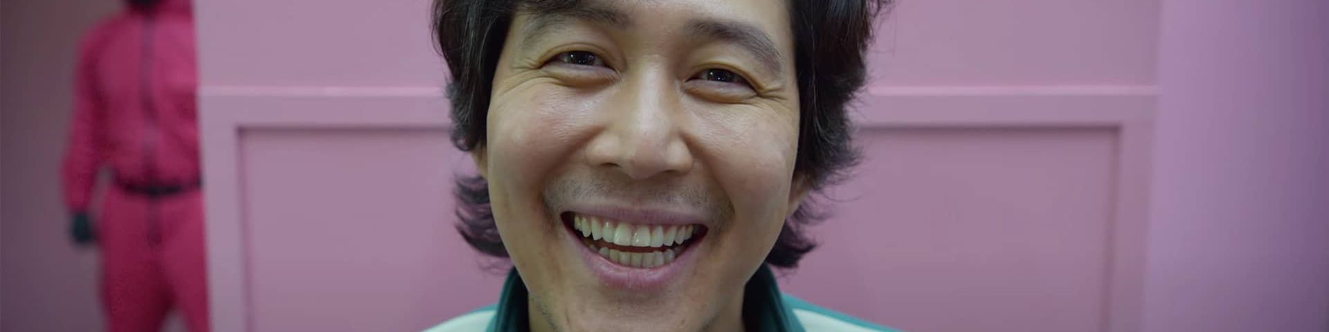le visage d'un homme coréen souriant devant un mur rose, Squid games