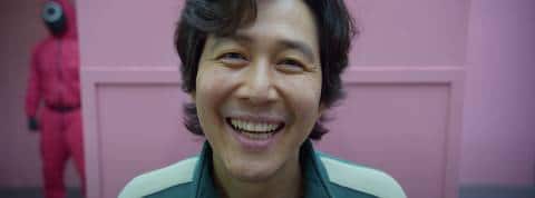 Squid Game envahit les réseaux le visage d'un homme coréen souriant devant un mur rose, Squid games