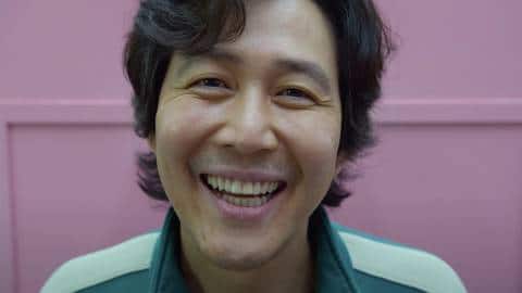 le visage d'un homme coréen souriant devant un mur rose, Squid games