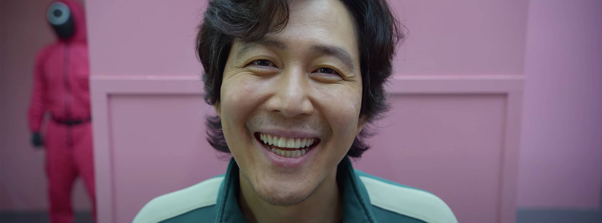 Squid Game envahit les réseaux le visage d'un homme coréen souriant devant un mur rose, Squid games