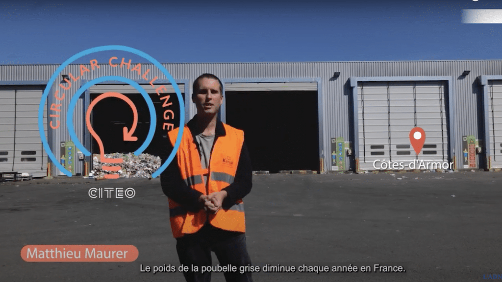 journaliste reporter face caméra devant un entrepôt dans une région ensoleillée