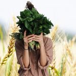 Jeune femme tenant des herbes devant son visage sur fond de champs de blé