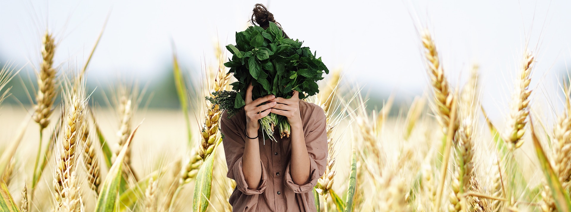 Vegan - L'ADN Jeune femme tenant des herbes devant son visage sur fond de champs de blé