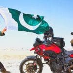 Rosie Gabrielle, influenceuse brandissant un drapeau pakistanais dans le désert, devant sa moto