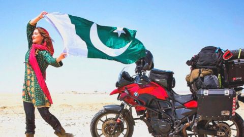 Rosie Gabrielle, influenceuse brandissant un drapeau pakistanais dans le désert, devant sa moto