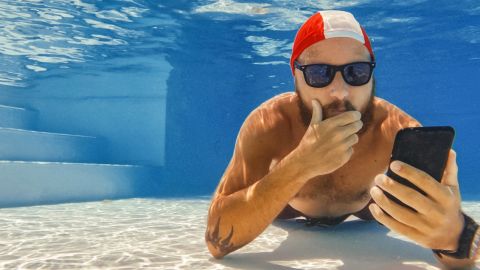 Homme au fond d'une piscine avec son portable