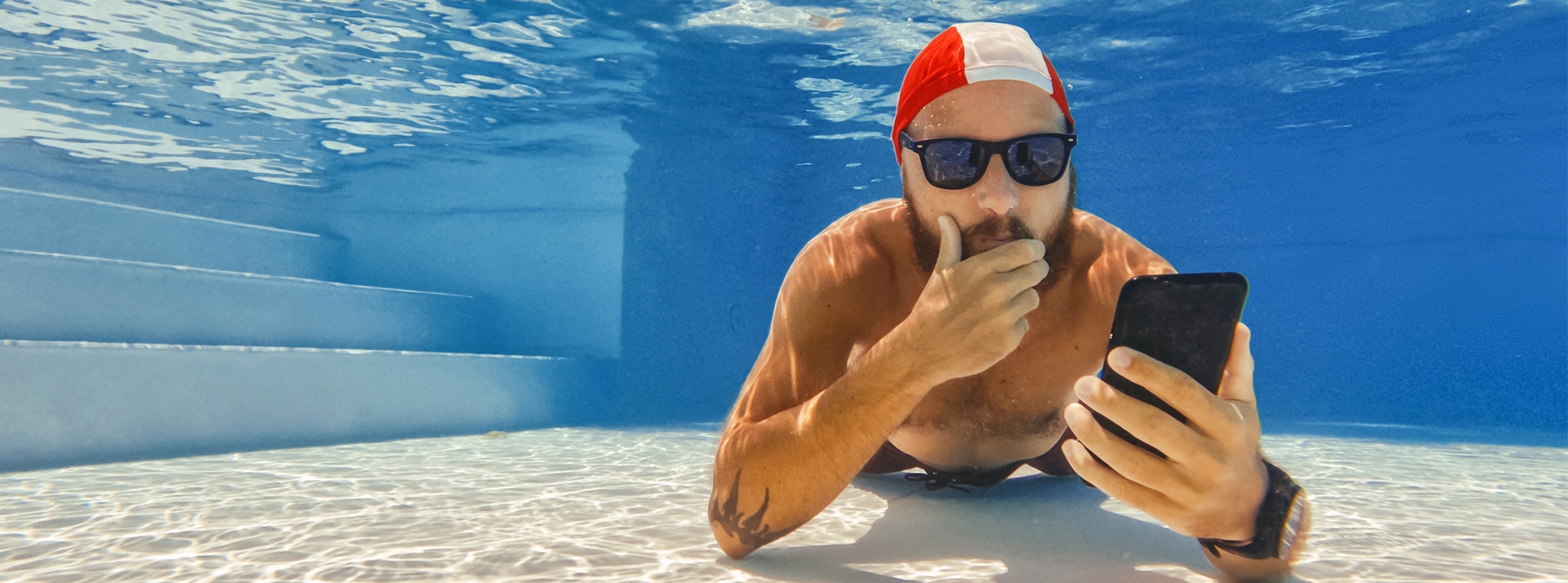 Homme au fond d'une piscine avec son portable