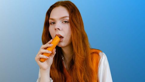 Jeune femme rousse croquant une carotte crue