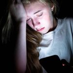 une jeune fille en pleur devant son portable dans le noir