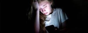 une jeune fille en pleur devant son portable dans le noir