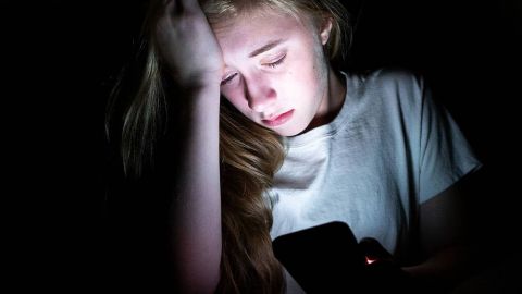 une jeune fille en pleur devant son portable dans le noir