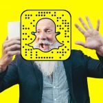 un homme de plus de 50 ans qui fait coucou devant son smartphone avec le logo de Snapchat