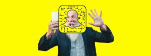un homme de plus de 50 ans qui fait coucou devant son smartphone avec le logo de Snapchat