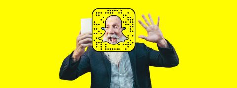 Snap un homme de plus de 50 ans qui fait coucou devant son smartphone avec le logo de Snapchat