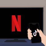 une personne regarde son smartphone branché sur TikTok tandis qu'une télévision affiche Netflix en arrière plan.