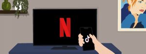 une personne regarde son smartphone branché sur TikTok tandis qu'une télévision affiche Netflix en arrière plan.
