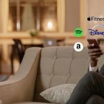 Un homme sur un canapé regarde son smartphone, des logos Spotify, Netflix, apple fit sont autour de son smartphone