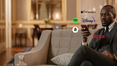 Un homme sur un canapé regarde son smartphone, des logos Spotify, Netflix, apple fit sont autour de son smartphone