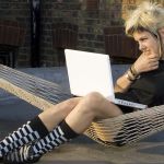 Jeune femme au look rock avec son portable, dans un hamacur un toit