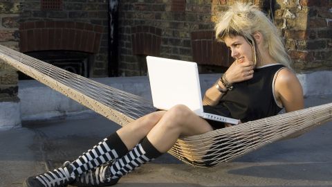 Jeune femme au look rock avec son portable, dans un hamacur un toit