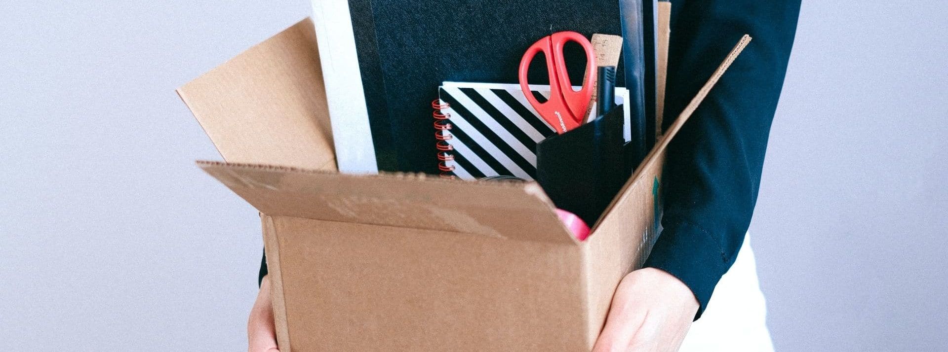 Personne tenant un carton dans ses mains avec ses affaires de bureau