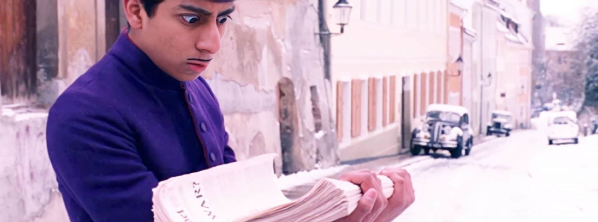 Les gens ne lisent plus les journaux d'info - L'ADN Capture de Grand Budapest Hotel de Wes Anderson avec un grrom qui porte une pile de journaux et fait les yeux ronds
