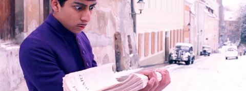 Les gens ne lisent plus les journaux d'info Capture de Grand Budapest Hotel de Wes Anderson avec un grrom qui porte une pile de journaux et fait les yeux ronds