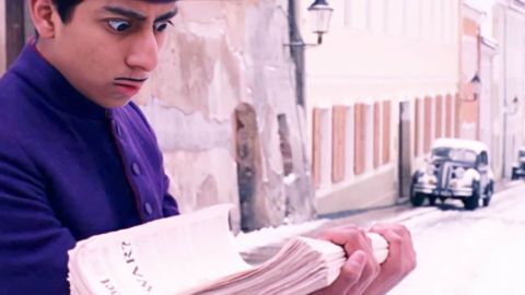 Capture de Grand Budapest Hotel de Wes Anderson avec un grrom qui porte une pile de journaux et fait les yeux ronds