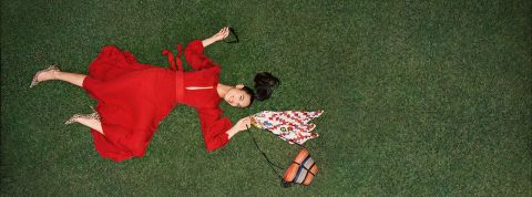 Le site de mode de luxe d'Amazon arrive en Europe Femme allongé sur une pelouse portant une grande robe rouge