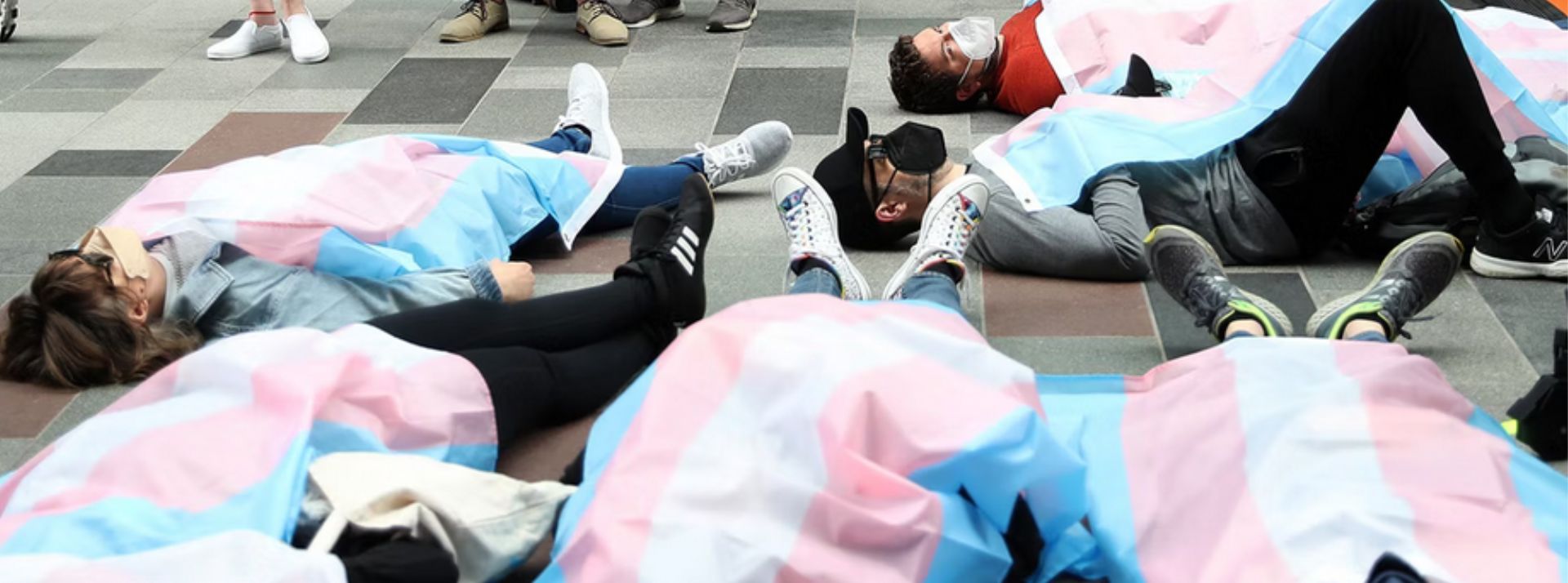 Les employés d’Amazon organise un die-in pour dénoncer pour la vente de livres transphobes - L'ADN Personnes allongées au sol, recouverte d'un drapeau LGBTQ