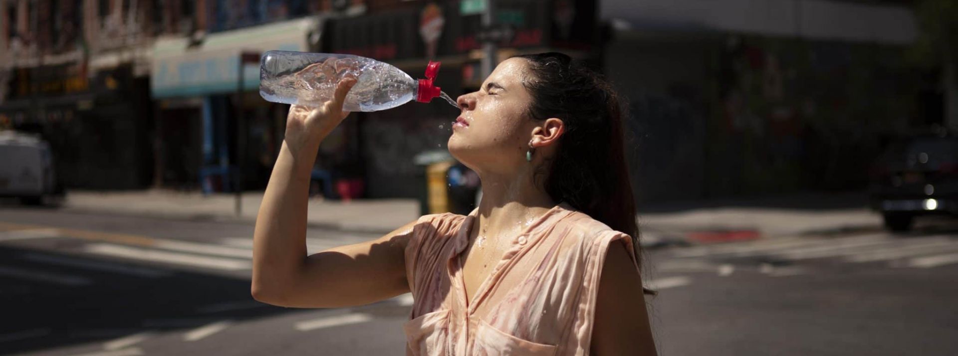 Canicule, changement climatique - L'ADN Jeune femme ayant très chaud se verse de l'eau sur le visage