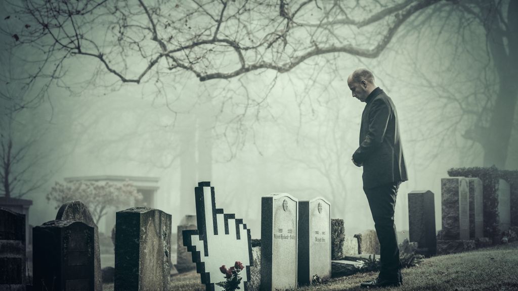 Man in graveyard by gravestone in the shape of a hand cursor