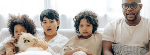 Enfants et écrans, on fait le bilan Un père et ses trois enfants assis sur un canapé qui regardent un écran