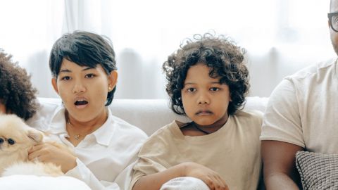 Un père et ses trois enfants assis sur un canapé qui regardent un écran